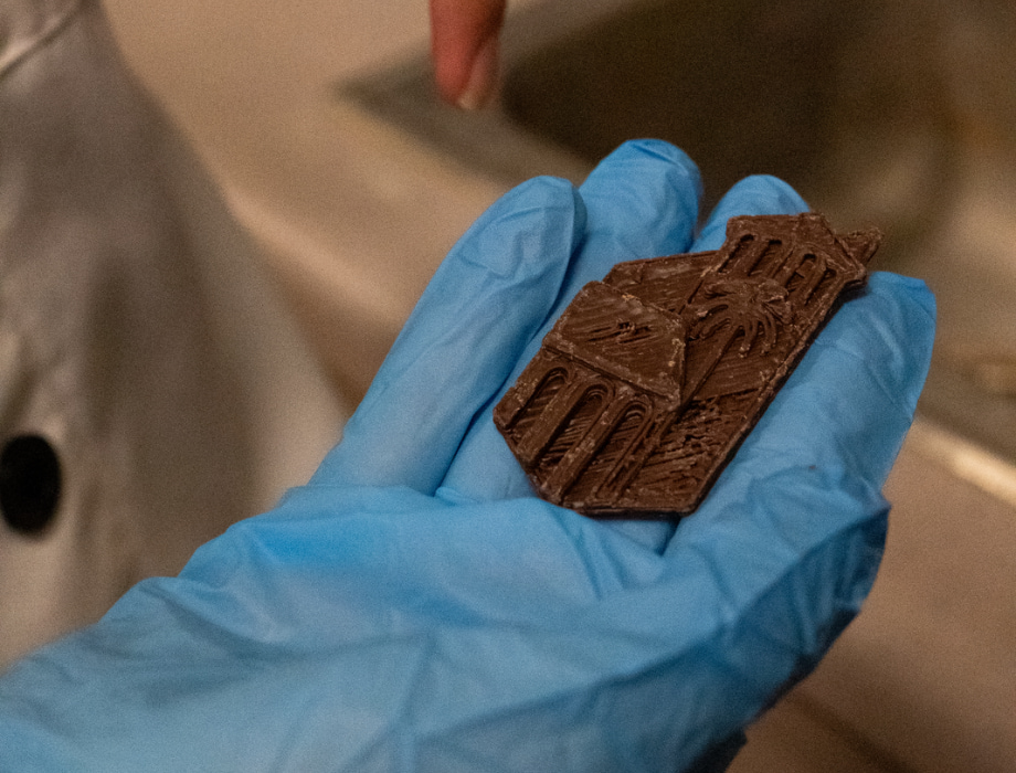 Blue gloved hand holding 3D printed chocolate in the shape of the CPP logo