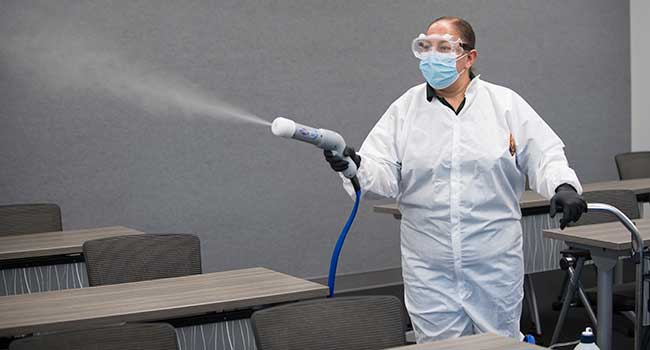 Custodian uses disinfectant sprayer to sanitize a classroom.
