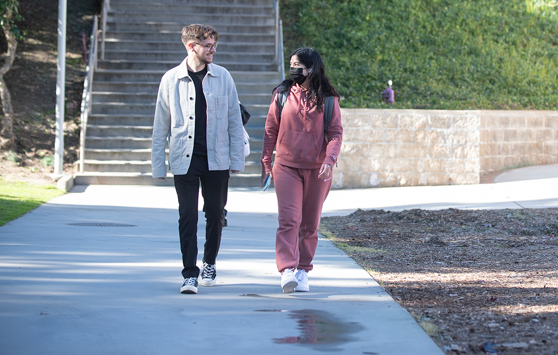 Male student and female student wearing a mask walk and talk together.