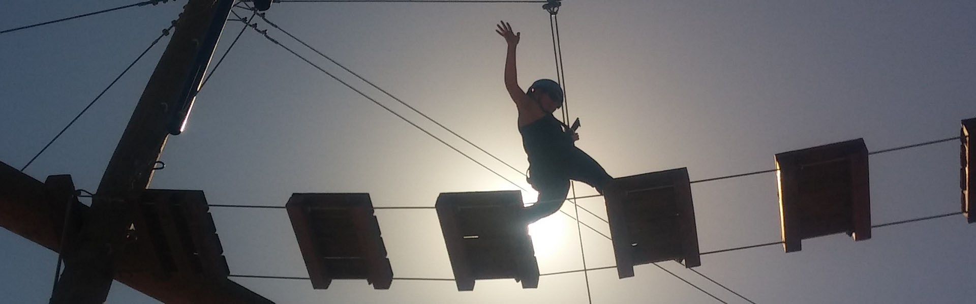 Student in rope-climbing gear walks across a wood plank bridge as part of a Challenge Ropes Course activity class offered by the Kinesiology department