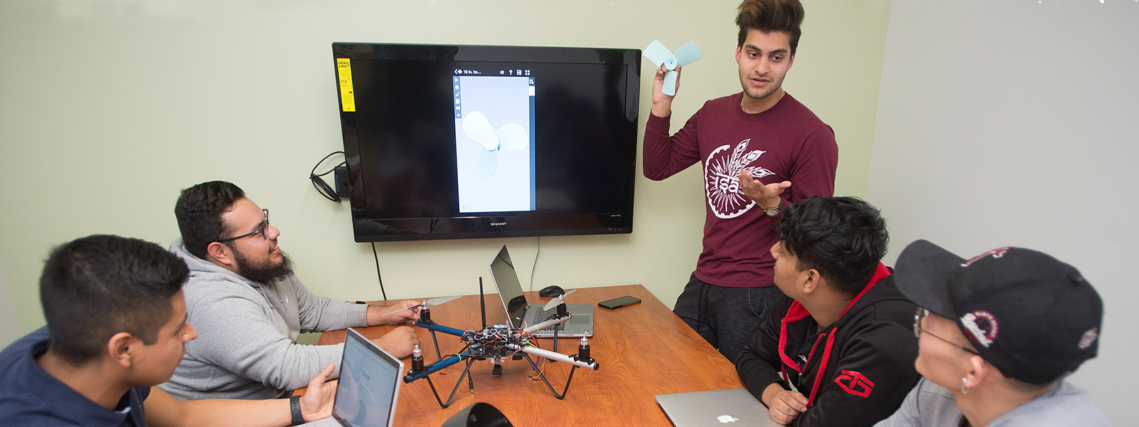 group discussing aerial tech parts at a table around a monitor