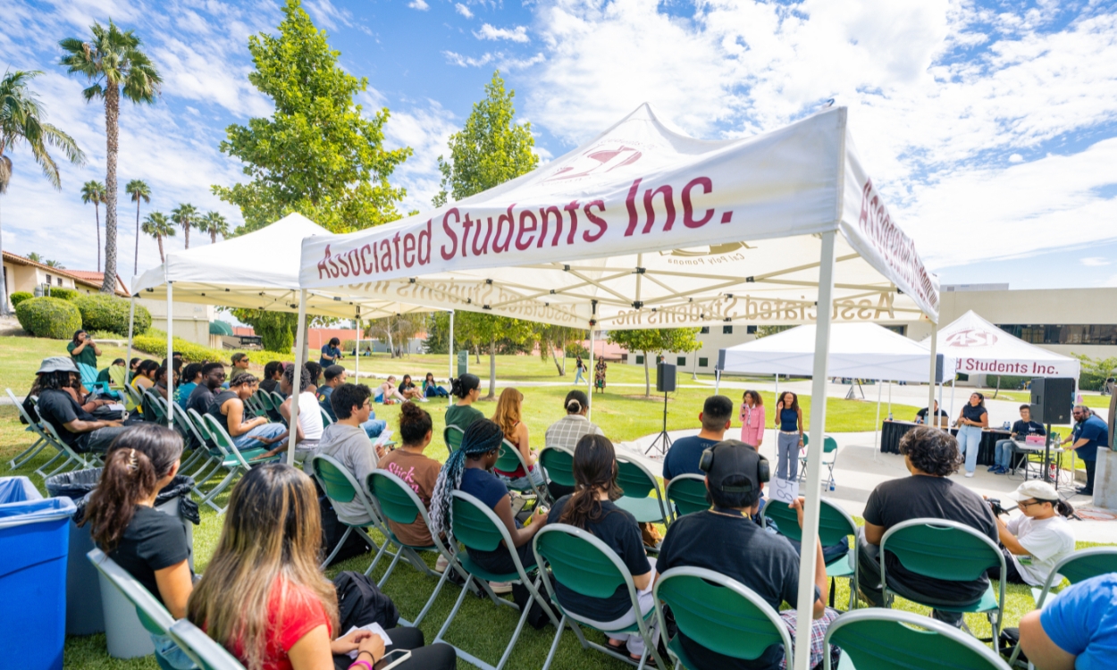 Students seated underneath a tent listen to the ASI president and vice president