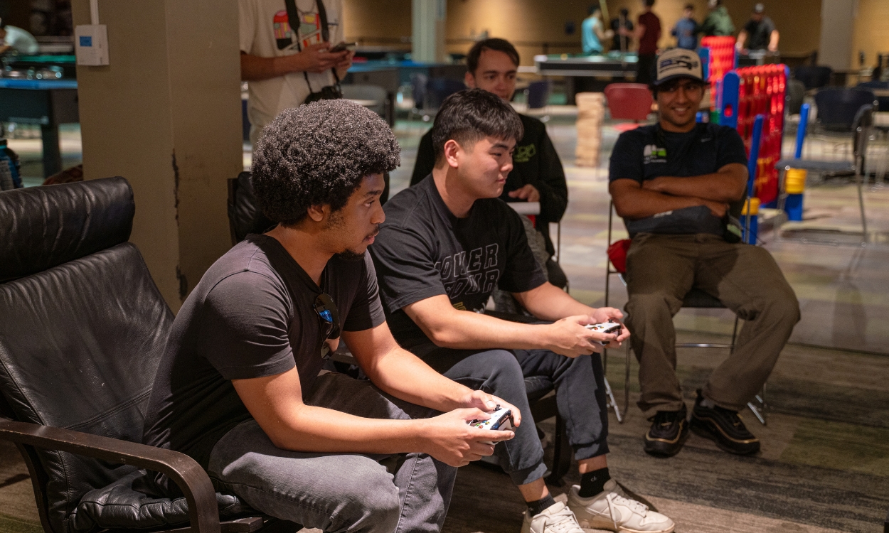 Two students holding PS5 controllers concentrate on the game.