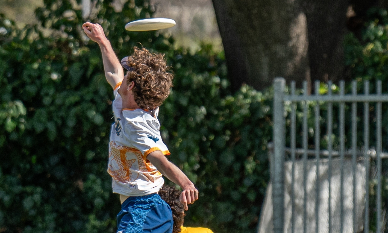 A student jumps in the air to catch a frisbee during an ultimate frisbee match.