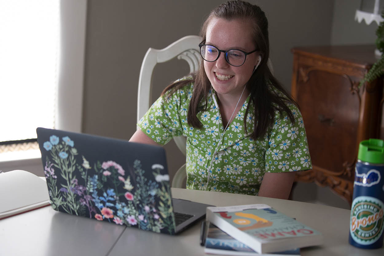 A female student looks and smiles at her laptop
