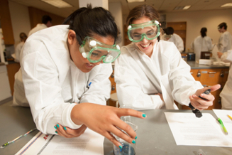Two female students in lab coats holding a beaker