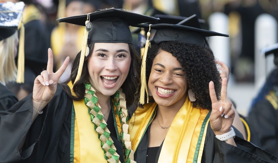 two students at Commencement put up peace signs