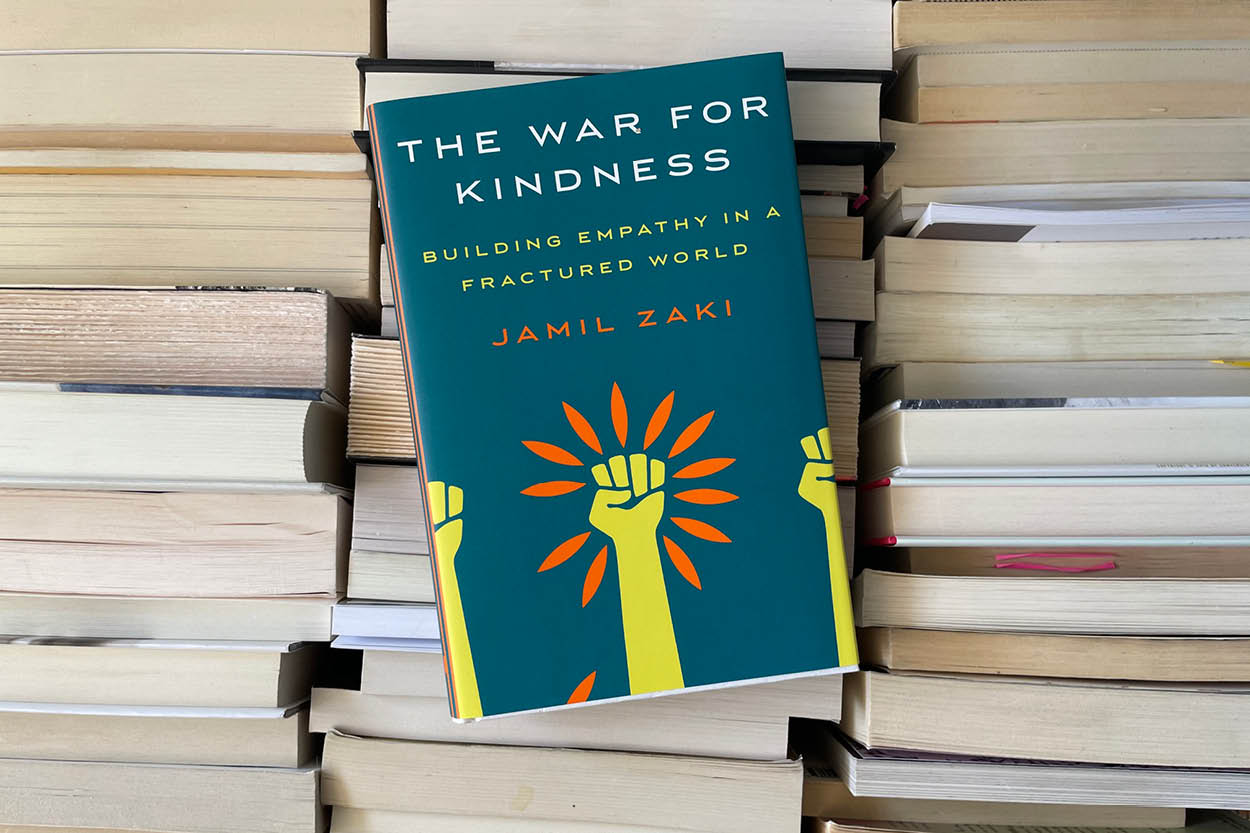 Photo of War on Kindness book laying on a background of book spines