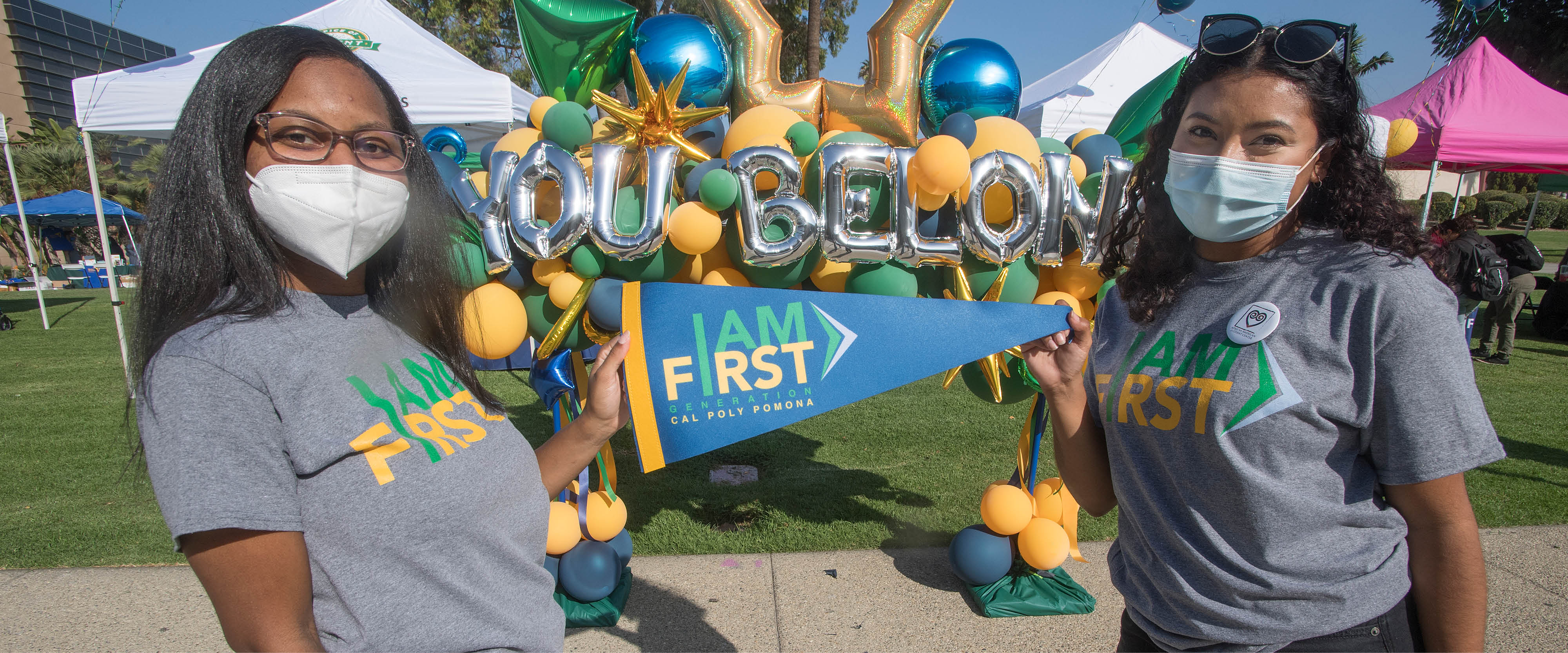 Two students hold up an I AM FIRST pennant at an on-campus event