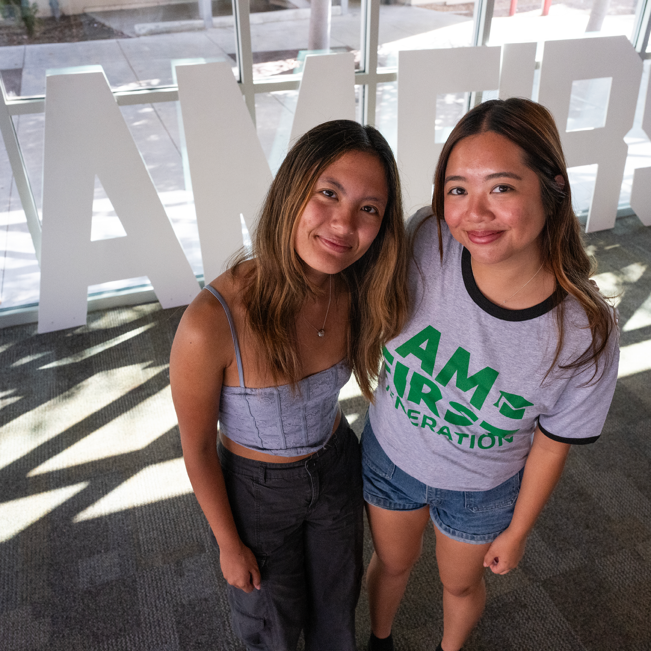 Two women students stand in front of I Am First sign
