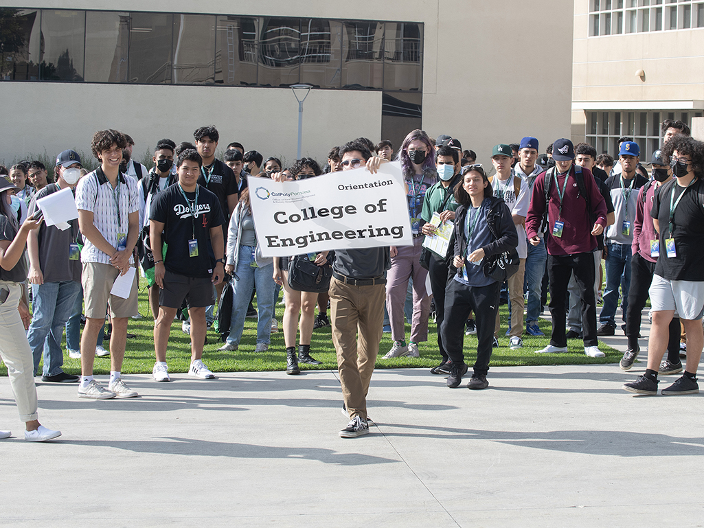 A student carrying a College of Engineering sign leads a group of students