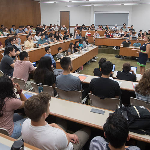 A photo of a CBA lecture hall -- students listen to a female instructor in the center of the room