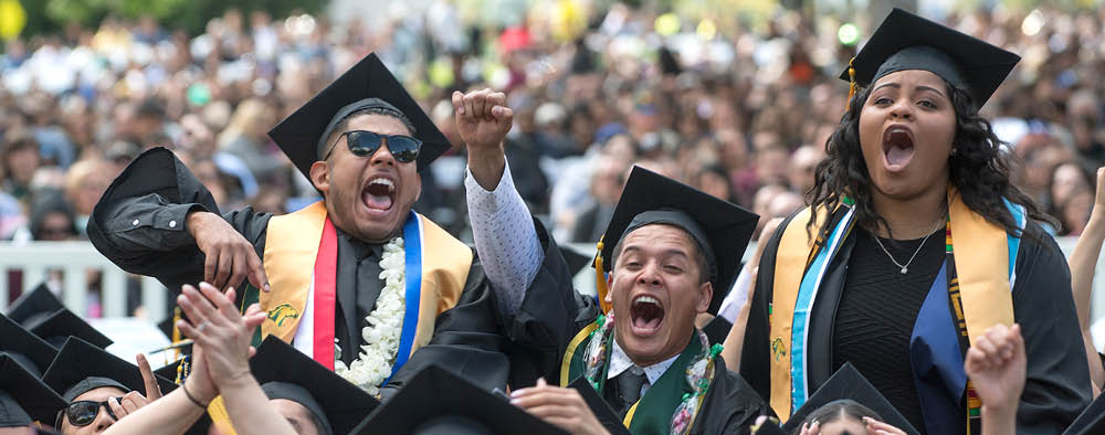 Three students, two male and one female, cheer at a Commencement ceremony