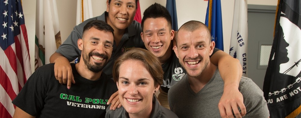 Veteran students pose for the camera in front of military flags