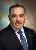 Headshot of a professional man in a suit with a blue tie looking at the camera.