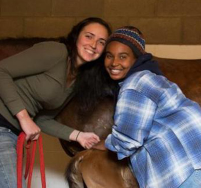 two students pose with a foal and mare icon