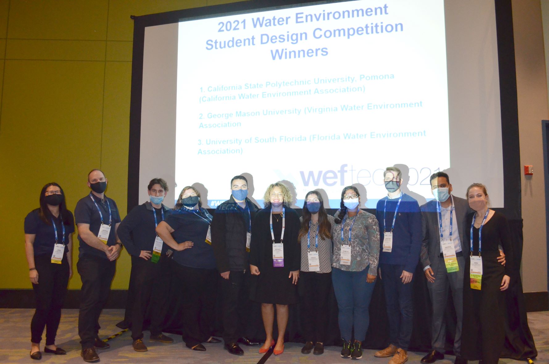 A group photo of 11 students standing in front a presentation, celebrating their victory in a student competition.
