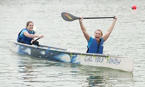 Two female engineering students in a canoe and celebrating with their arms in the air.