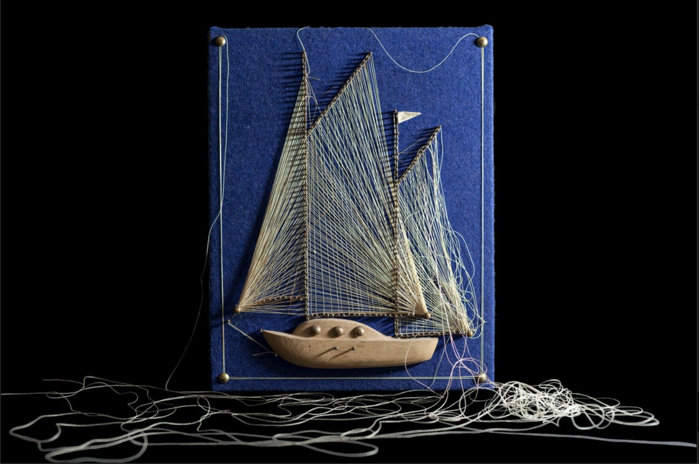 Blue fabric canvas with a boat embroidered into it with string on the floor 