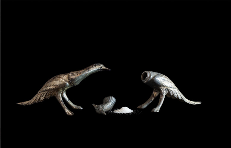 two metallic birds faced to one another, right bird head is of with salt next to it