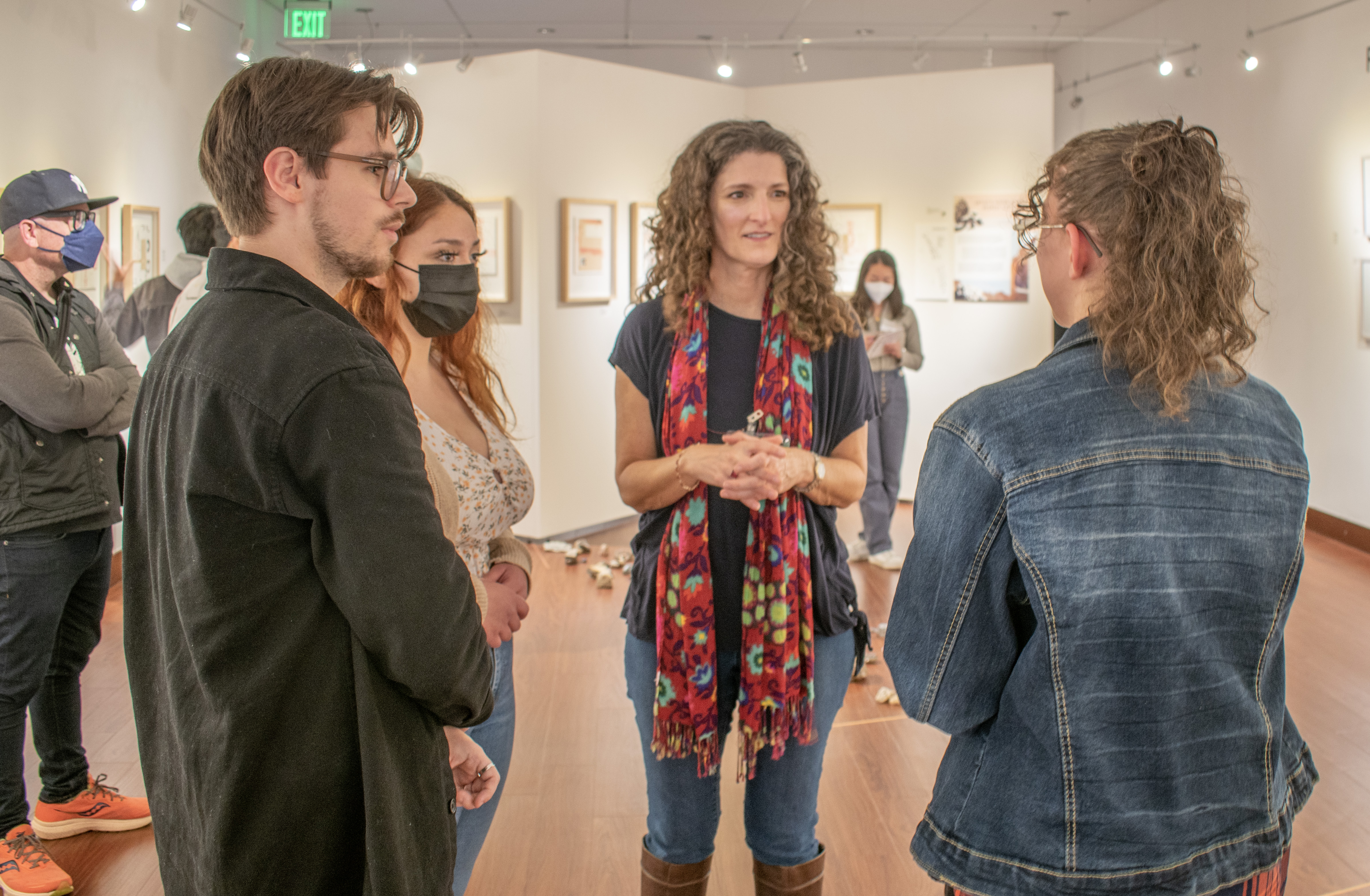 A photo of Sarah Meyer talking to two guests during her opening exhibition. She is in the middle of the two guests, and she is talking and making eye contact with the one on her left.