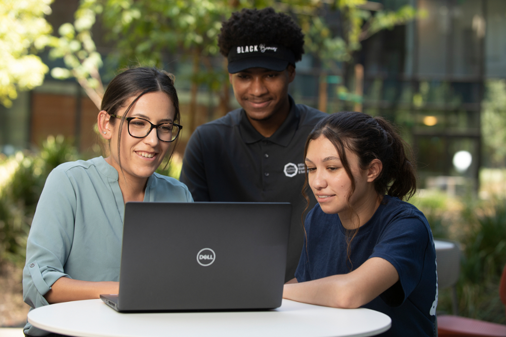 Two female students and one male work together on a laptop outdoors 