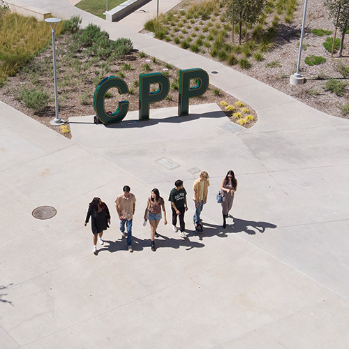 A group of student walk by the green CPP letters by the park at 98.