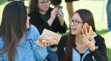 Two female students talk and eat hot dogs during the 2019 Hot Dog Caper.