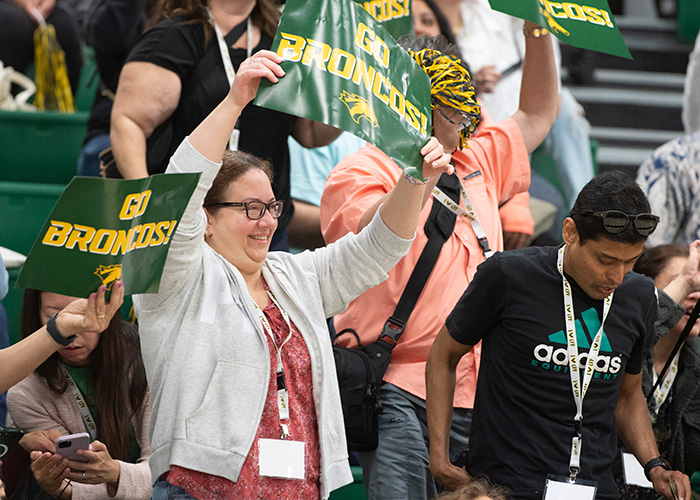 A female parent celebrates holding a sign that says Go Broncos.