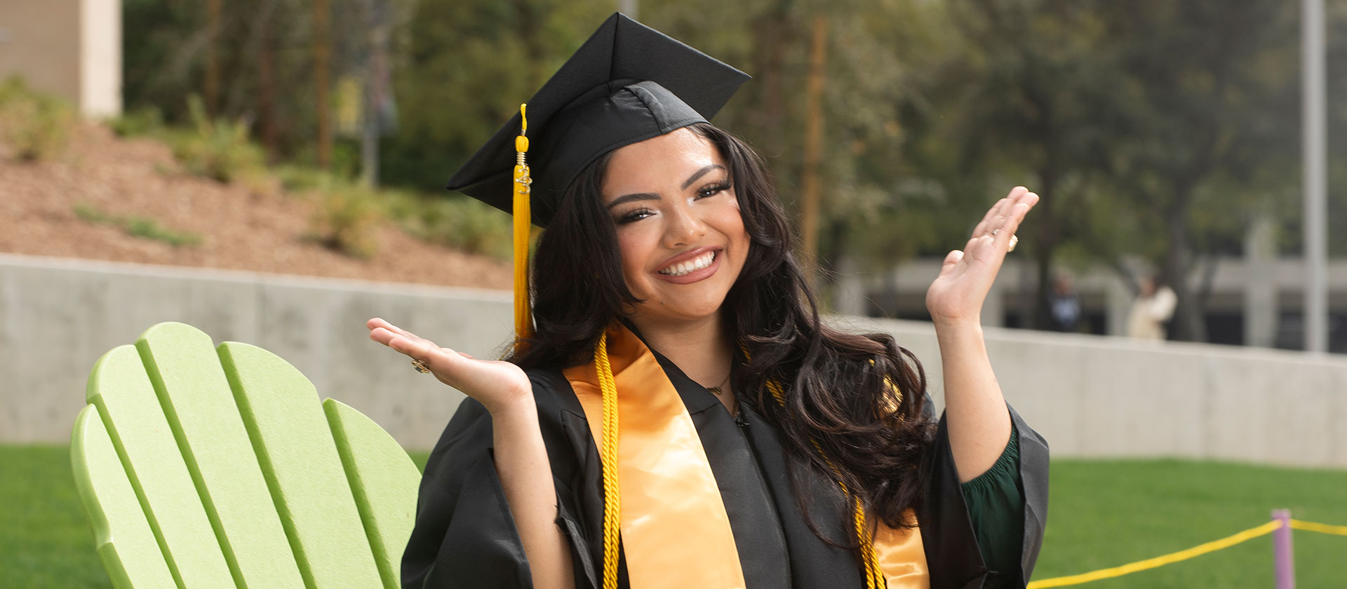 Diana Aguilar-Cruz smiles while sitting in her cap and gown on a chair.